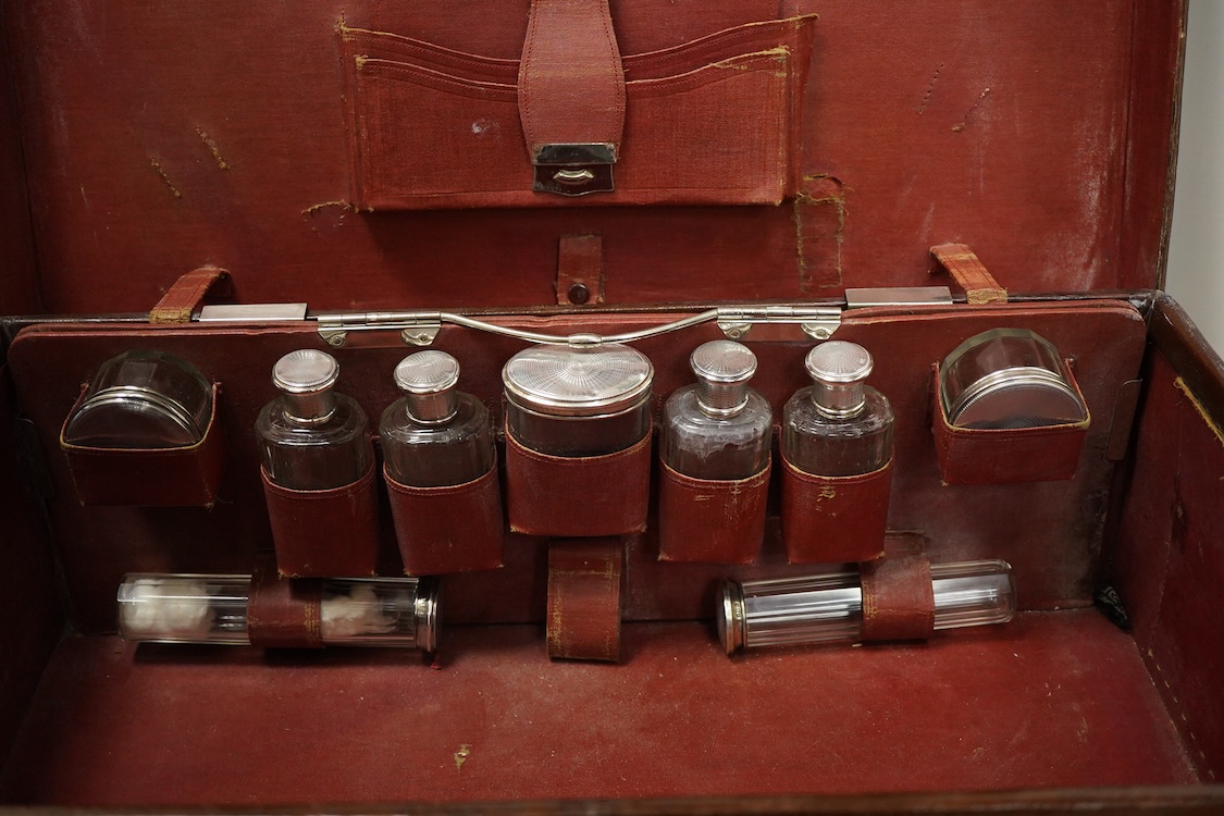 An early 20th century leather travelling toilet case, with 'Peninsular & Oriental Steam Navigation Compy' paper labels, containing eight French 950 standard white metal mounted glass toilet jars and one English silver mo